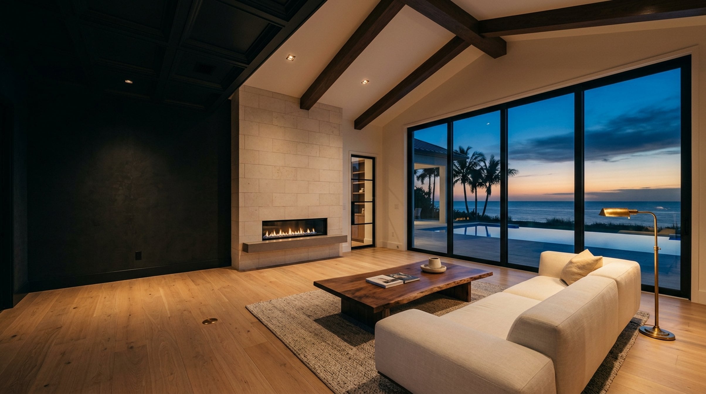 Coastal-contemporary Moose Homes great room at twilight — floor-to-ceiling hurricane-impact glass, warm white oak floors, limestone fireplace.